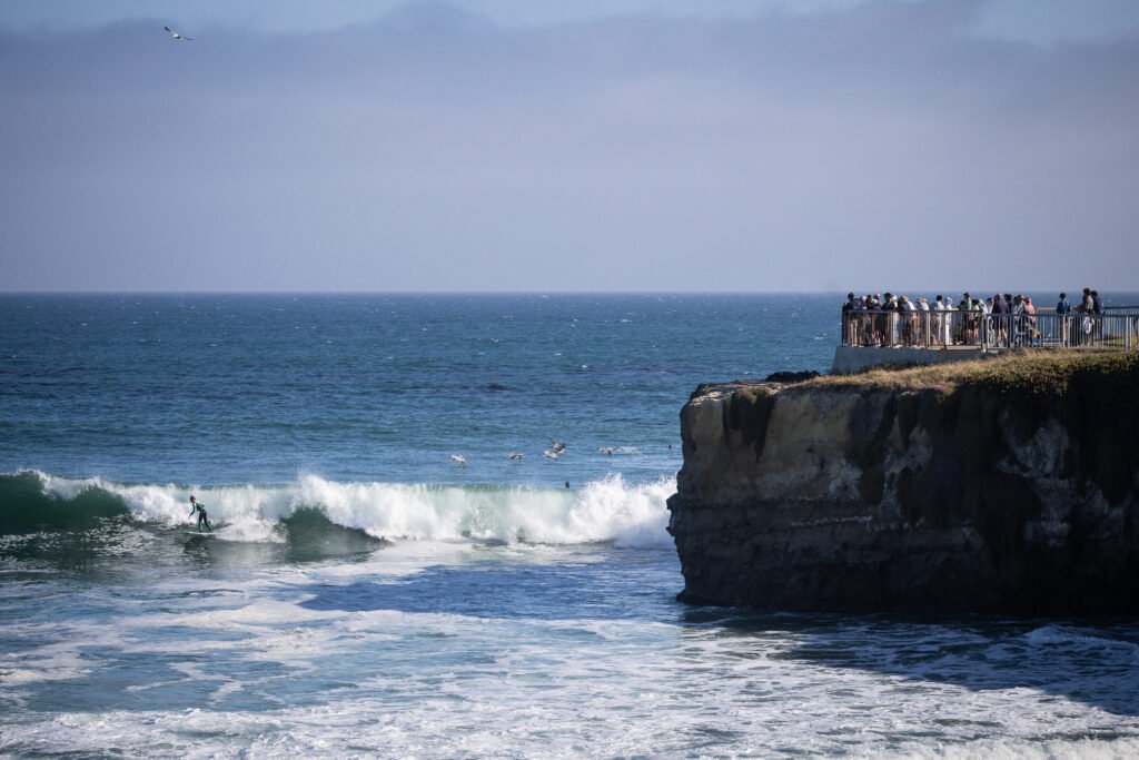 Surfer riding a wave with spectators on a cliff at Steamer Lane, Santa Cruz, California, USA